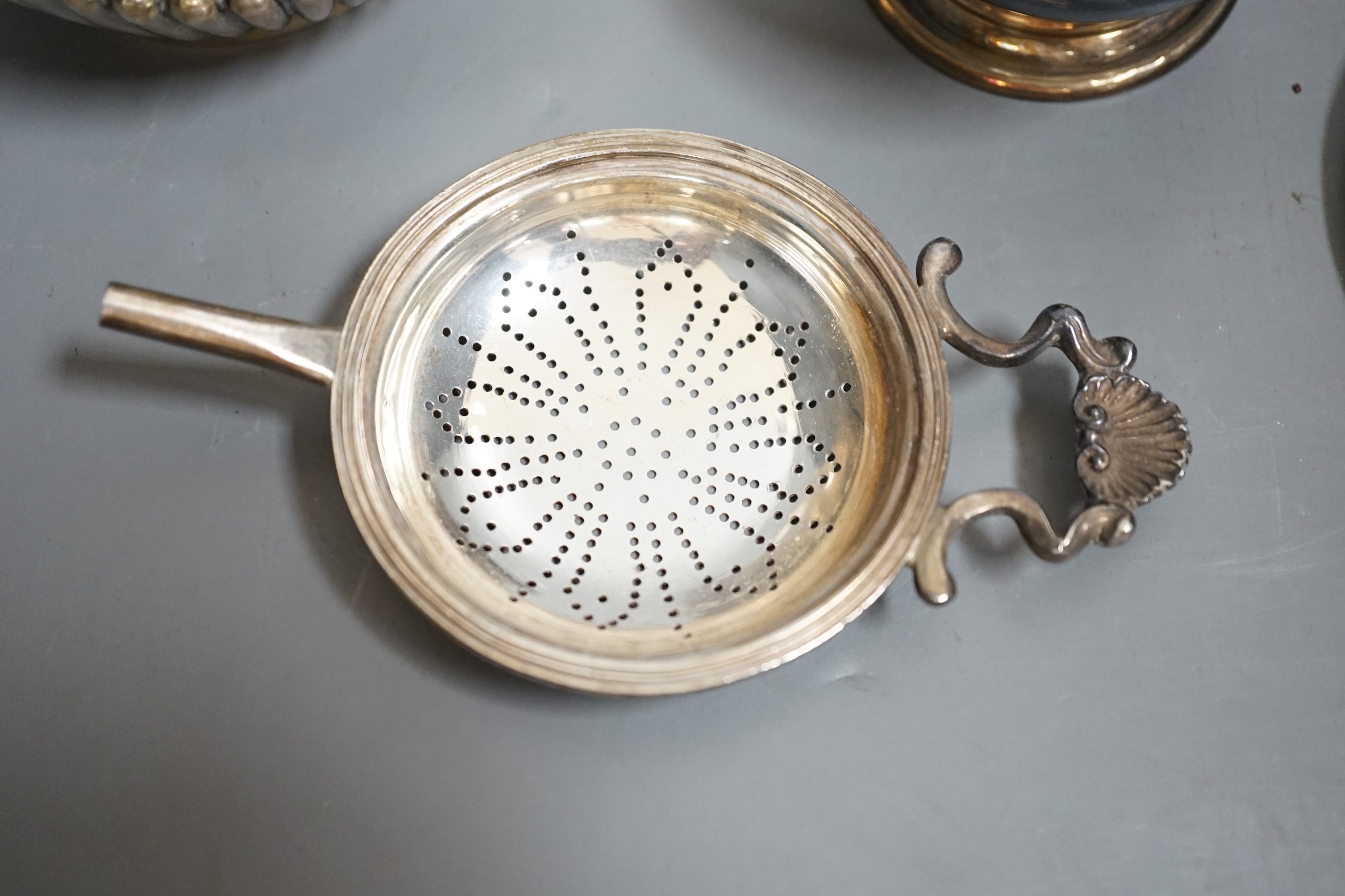A late Victorian silver half-fluted tea caddy, Birmingham, 1900, a silver strainer on stand, a silver egg cup stand and a pair of silver server spoons.
